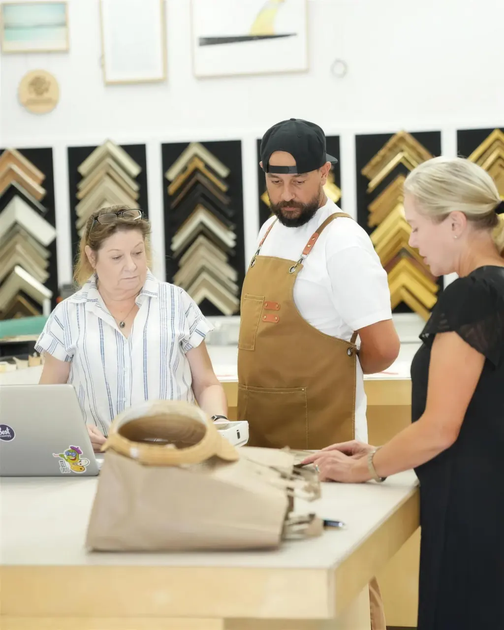 A consultation at the Best Framing design counter, moulding samples on the wall behind