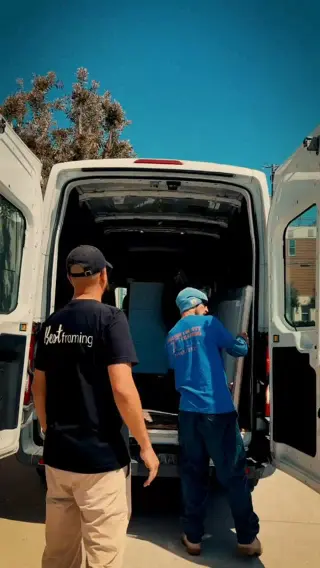 Two of the team at the open rear doors of the van, loading finished work