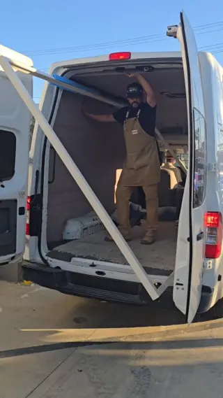 One of the crew standing in the back of the van, an oversized frame angled out through the open doors