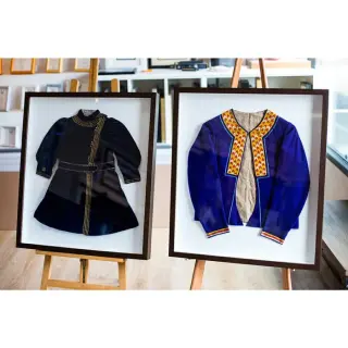 Two antique children's garments in dark-wood shadow boxes, on easels in the showroom