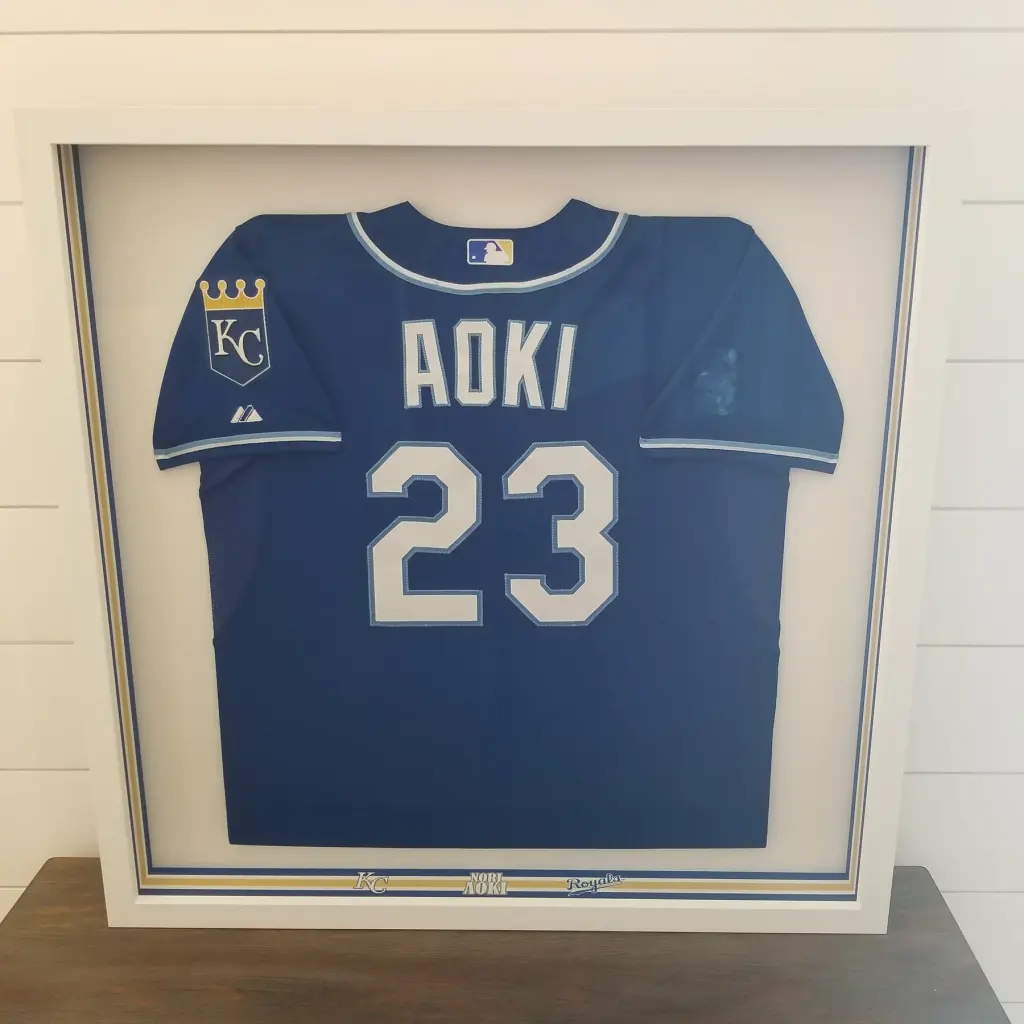A blue Aoki number 23 baseball jersey in a white shadow box, the mat lined in navy and gold
