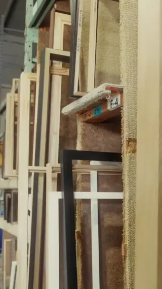 Joined frames standing on end in the shop rack, light oak, black and white profiles side by side under a bay label