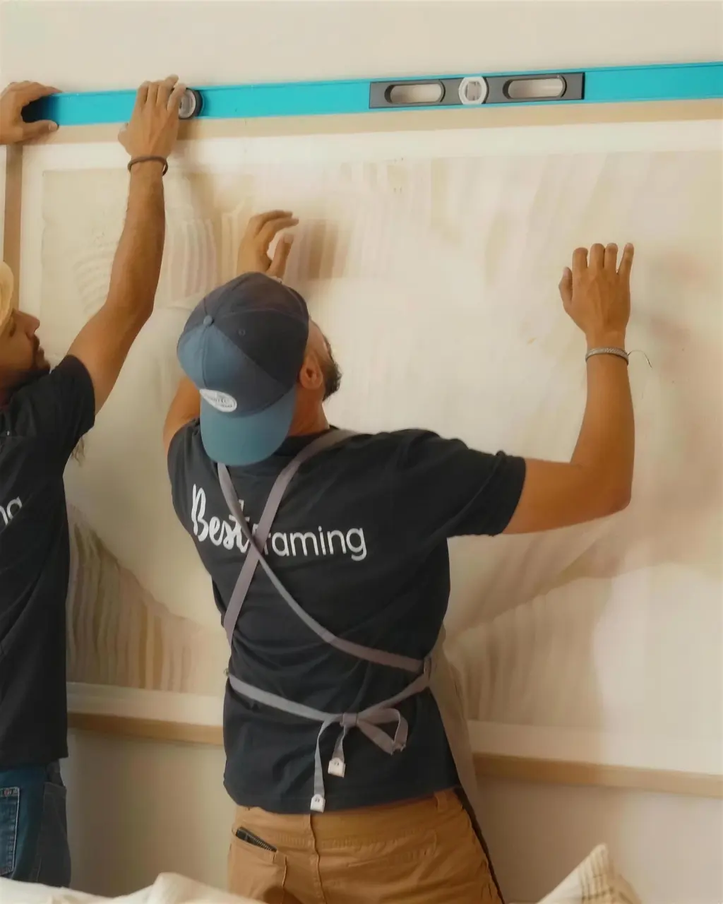 Two installers levelling a large framed piece on a client wall