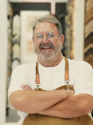 Chris in a canvas apron, arms crossed, in the showroom
