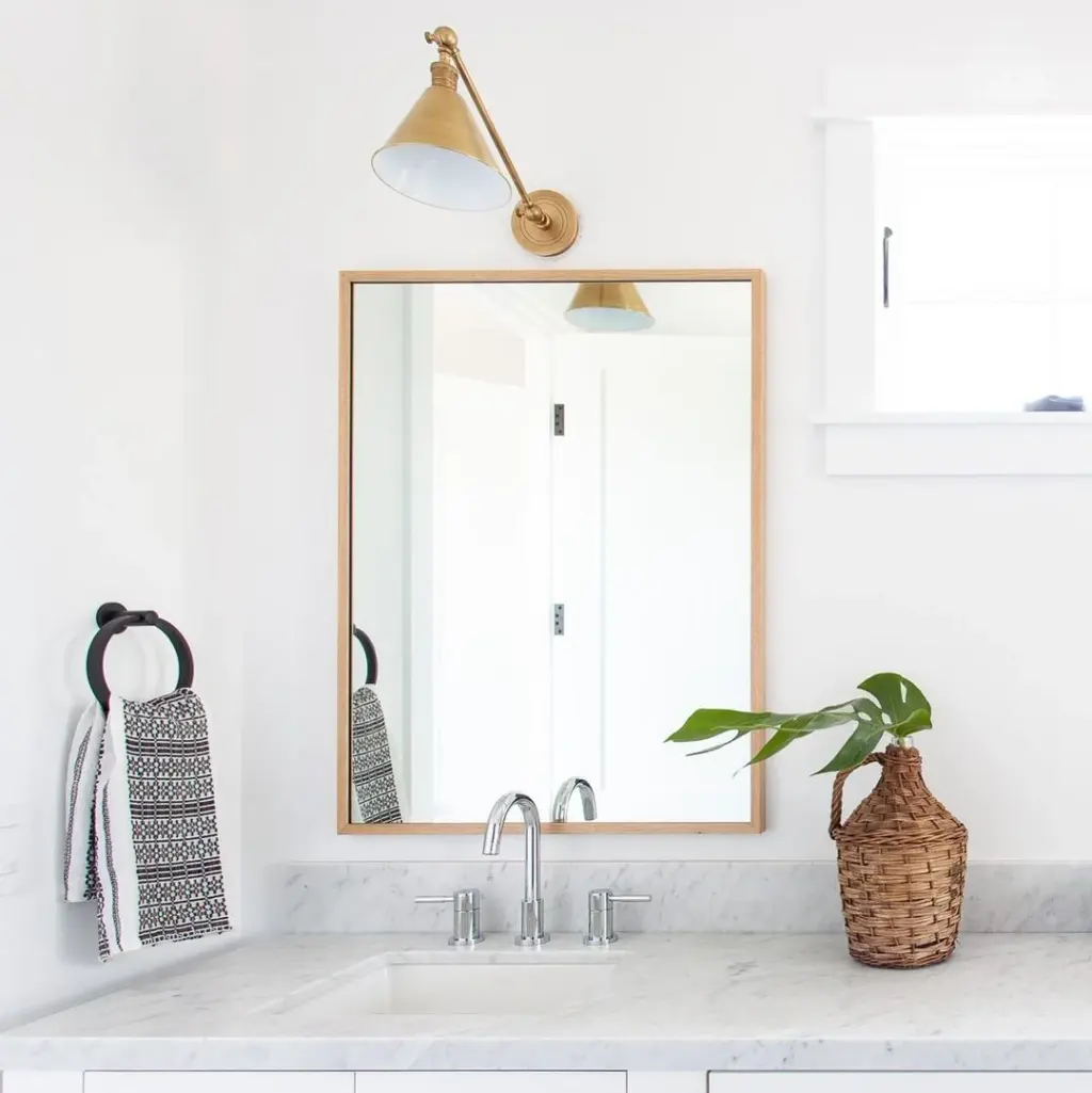single light oak framed mirror with a brass swing arm sconce, marble counter