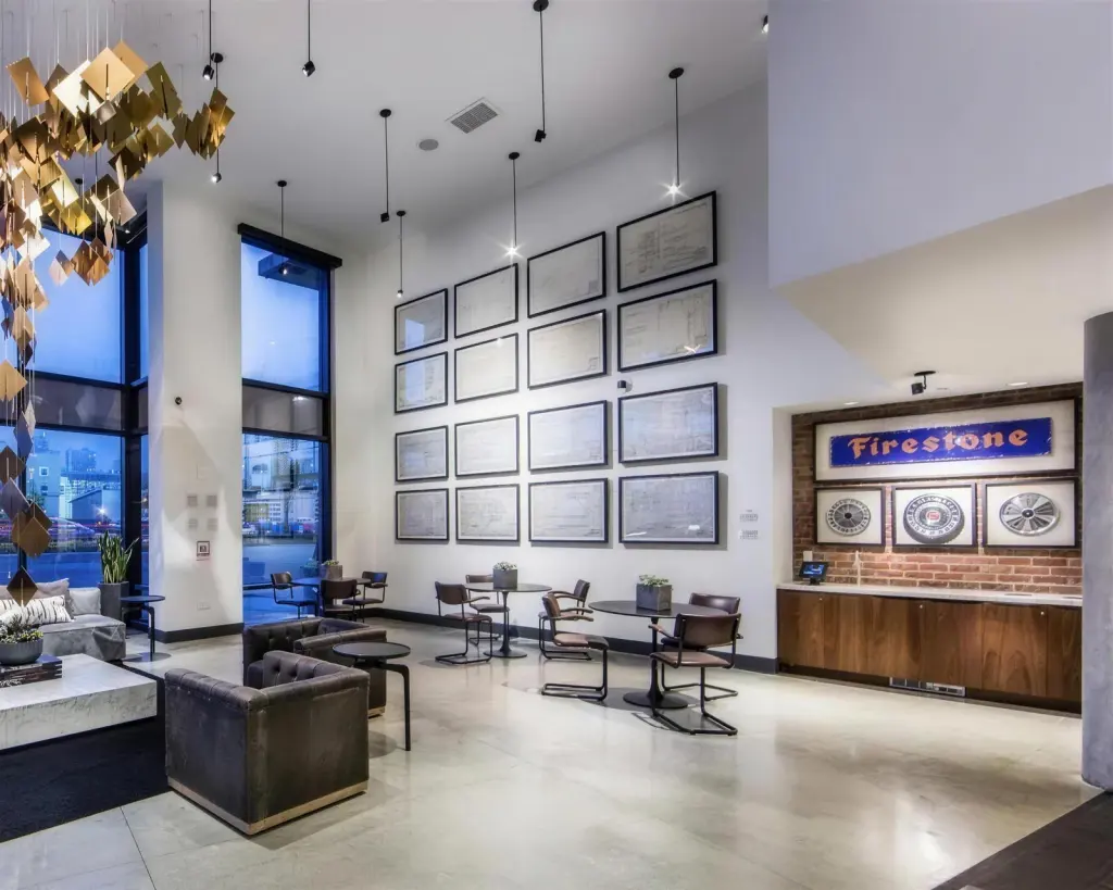A double-height lobby wall hung with sixteen black-framed archival blueprints in a grid, with three shadow-boxed hubcaps on brick below