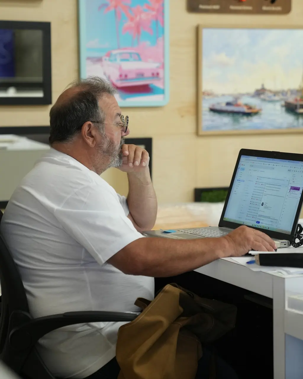 A Best Framing team member at a computer in the showroom, hand to his chin, reviewing a file on screen, framed art on the wall behind him