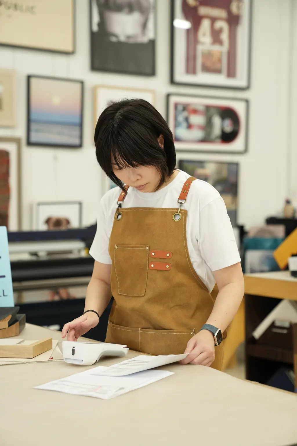 A designer checking an order at the counter, framed jerseys and records on the wall behind