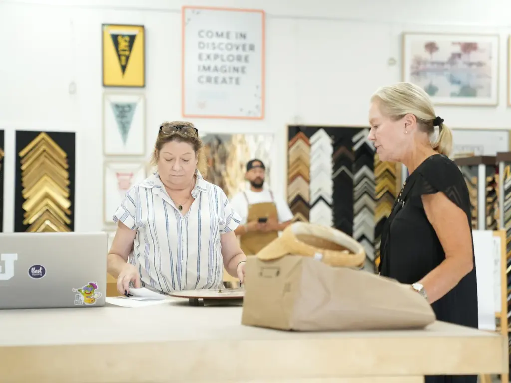 A customer and a framer working out a piece at the Best Framing design counter, moulding samples on the wall behind them