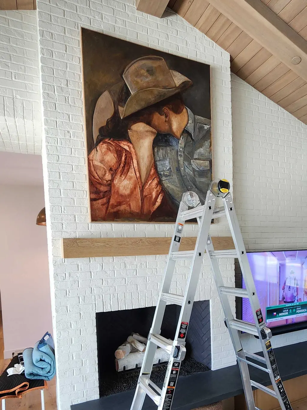 A large painting hung over a white brick fireplace, the installer’s ladder beside it