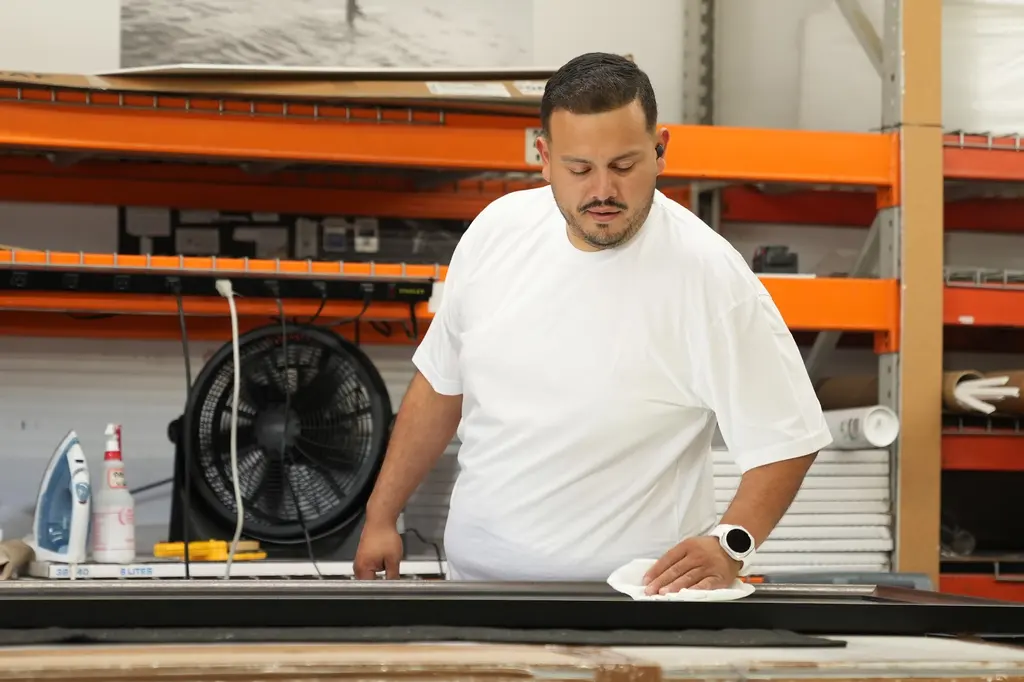 A framer cleaning the glass of a long black frame before it is closed up