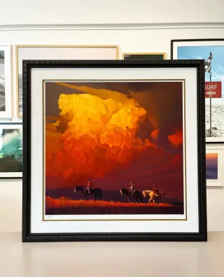 A signed print of an orange thunderhead over three riders, in a carved black chevron frame with a gold fillet and a wide white mat