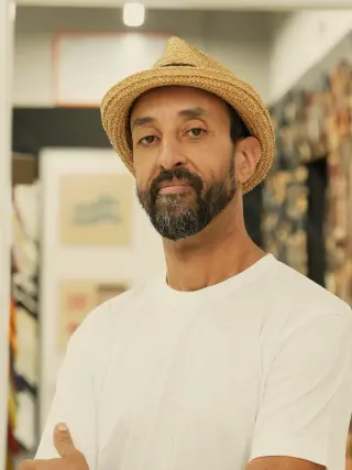 Karim in a straw hat, arms crossed, beside the moulding wall