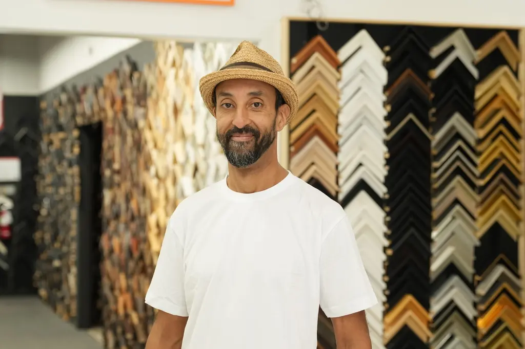 Karim in a straw hat in the Best Framing showroom, the moulding walls behind him