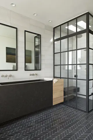 two black steel framed mirrors above a dark stone trough sink, steel shower cage