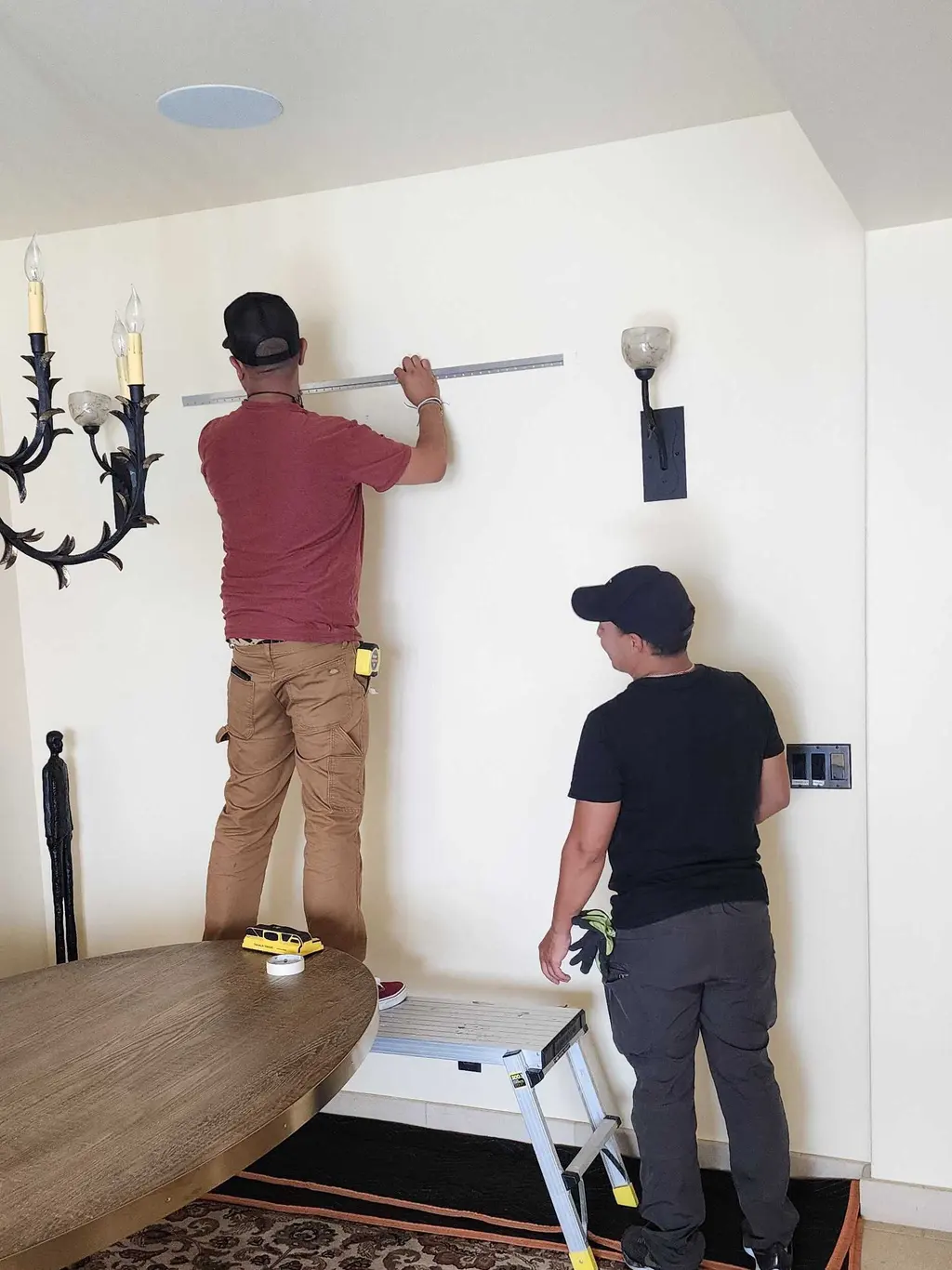 Two installers measuring and marking a dining room wall before hanging