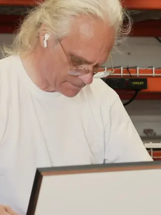 Michael holding a black frame with a white mat at the bench