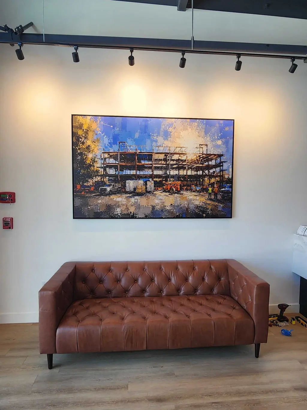 A large framed print under track lighting, over a leather sofa in an office lounge