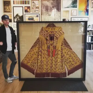 A gold and oxblood embroidered ceremonial robe floated in an ornate dark frame, held upright on the showroom floor