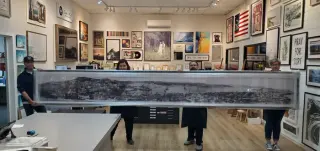 Four staff carrying a very long black-and-white harbour panorama across the showroom