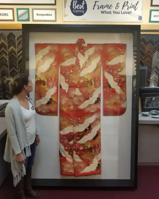Red silk kimono with white cranes floated in a tall black shadowbox, a woman looking up at it
