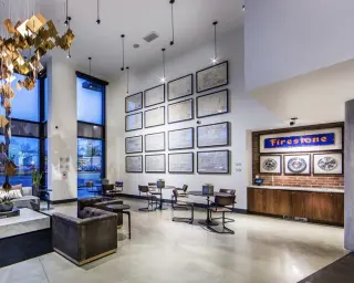 A double-height lobby hung with a grid of sixteen black-framed archival drawings above café tables, shadow-boxed hubcaps on the brick