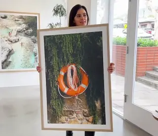 A large photograph framed in light oak with a white mat, carried through a bright gallery hung with more framed prints