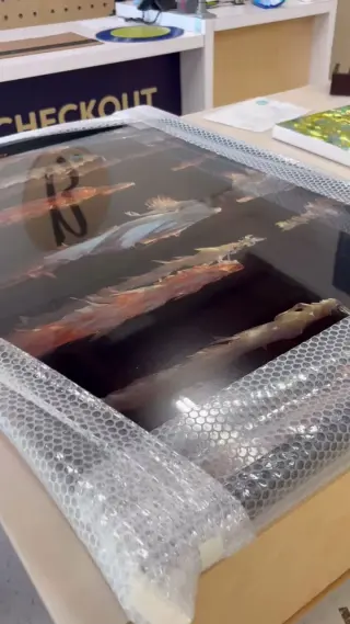 A large framed print wrapped in bubble wrap on the counter at Best Framing, the showroom checkout sign behind it