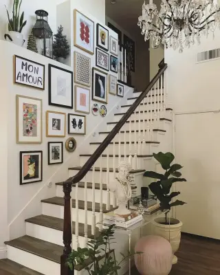 A dense salon-style gallery wall of mixed black, gilt and natural frames climbing a white stairwell