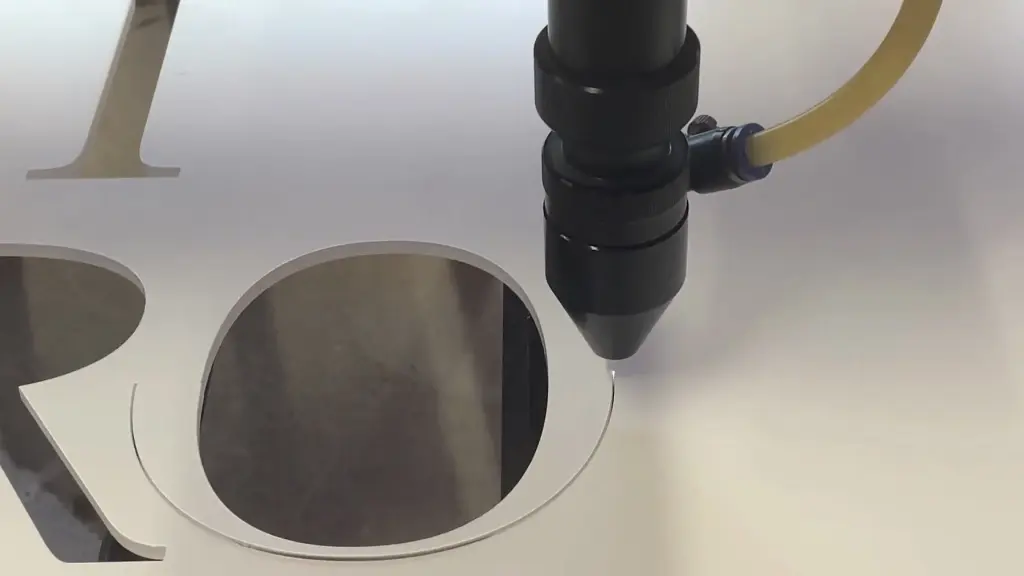The laser head tracing the curve of a letter O out of a white acrylic sheet, other serif letterforms already cut beside it