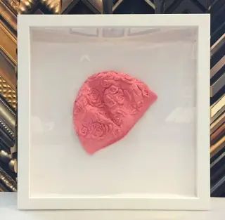 Pink rosette baby bonnet floated in a white deep shadow box