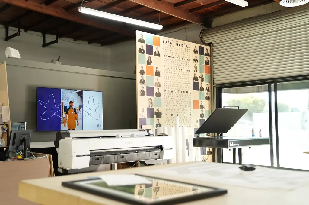 The print room, a wide-format printer by the open roll-up door and a framed piece on the table