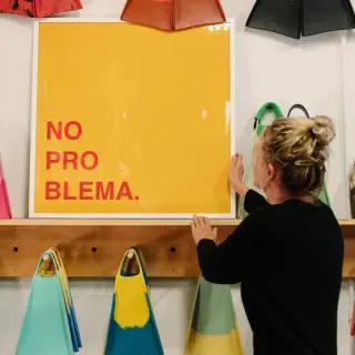 Framer holding a yellow and red NO PROBLEMA print against a wall of swim fins