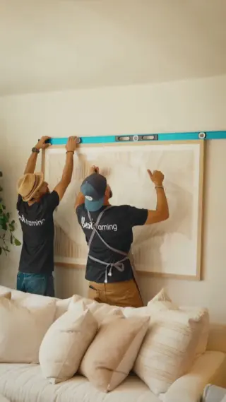 Two Best Framing installers levelling a large oak-framed abstract above a sofa