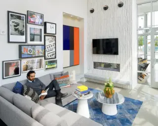 A model living room with a salon-style gallery wall of photographs, an On Air sign and sheet music over a grey sectional
