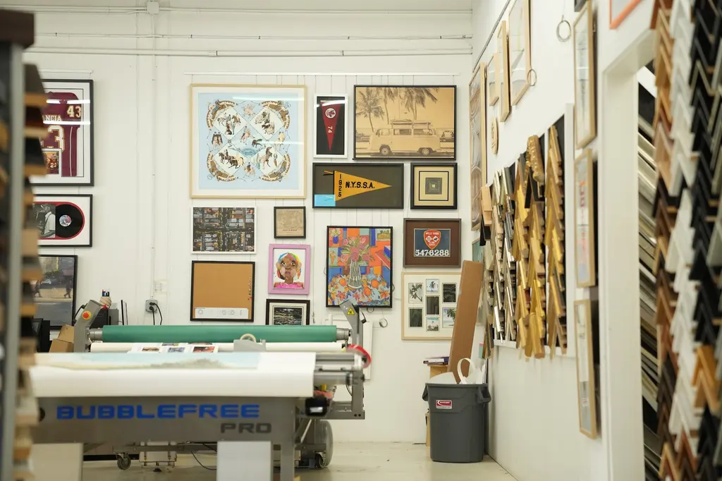 A room of the shop hung salon-style with framed pieces, the Bubblefree mounting press in front of the wall