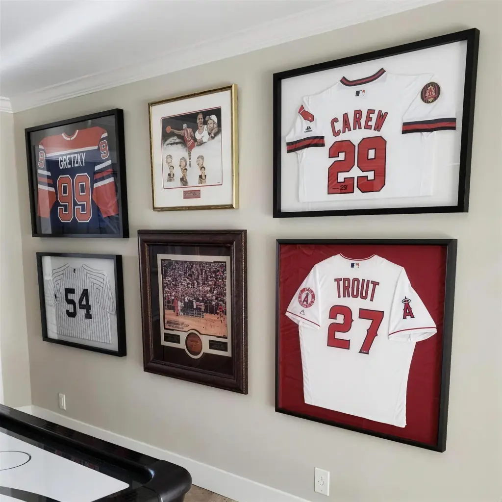 A games room wall of framed sports memorabilia, four signed jerseys in deep shadow boxes and two framed photographs between them