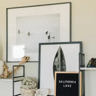 Two black-framed surf prints leaning on a shelf against a warm oat wall
