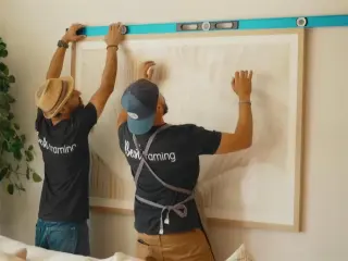 Two installers levelling a large framed piece on a client wall