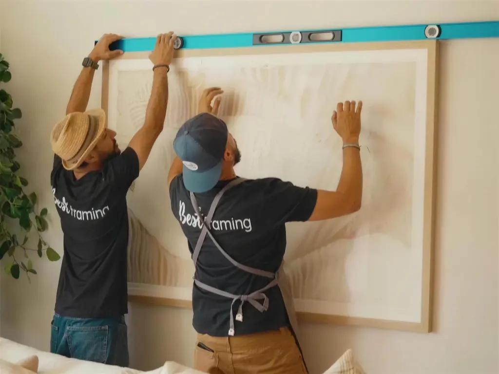 Two of the Best Framing crew holding a long level across the top of a large framed piece as they set it on a client wall
