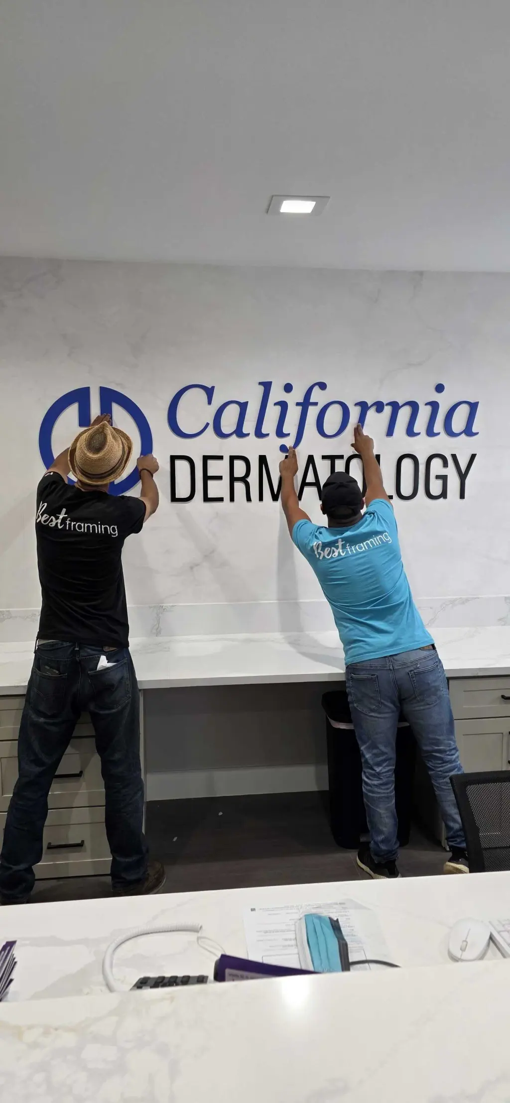 Two Best Framing installers setting dimensional blue and black lettering on a marble reception wall