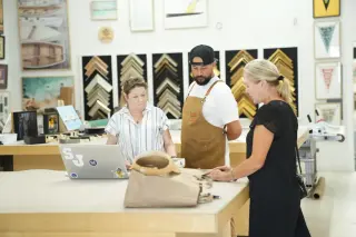 A consultation at the Best Framing design counter, moulding samples on the wall behind