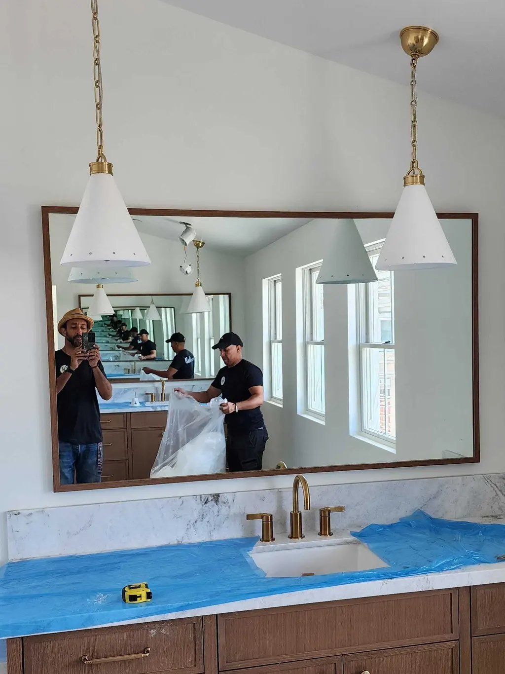 A wood-framed mirror installed over a bathroom vanity, the installers reflected in it