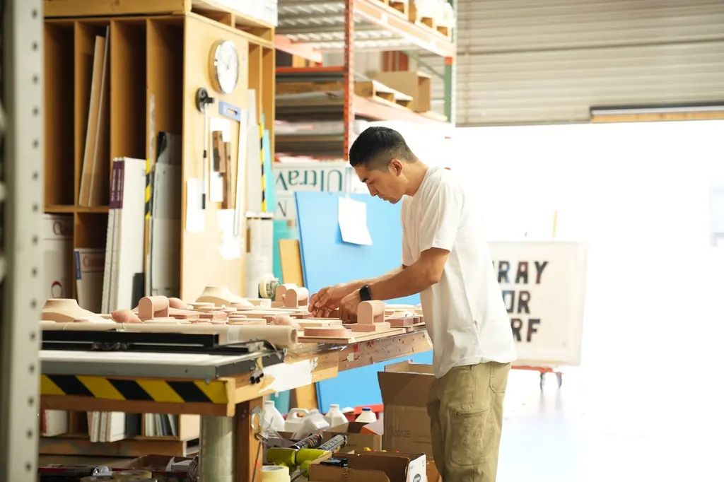 A woodworker at the bench in the wood shop, the roll-up door open behind him